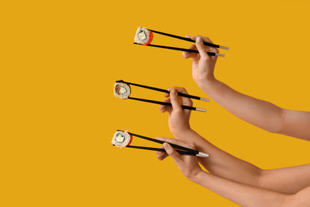 Female hands holding chopsticks with different tasty sushi rolls on yellow backgroundの写真素材
