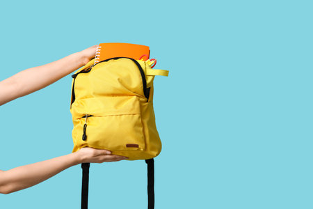 Female hands with backpack and different school supplies on blue background, closeupの写真素材