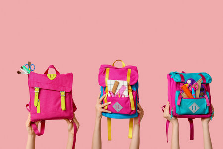 Female hands with backpacks and different school supplies on pink background, closeupの写真素材