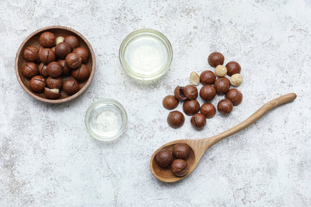 Composition with bowls of macadamia oil and nuts on light background