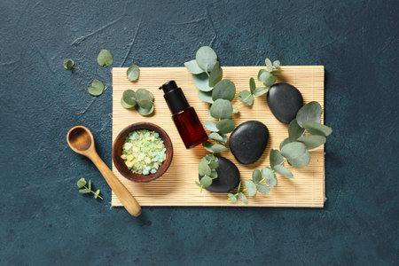 Spa stones, bamboo mat and bottle of eucalyptus essential oil on dark blue background