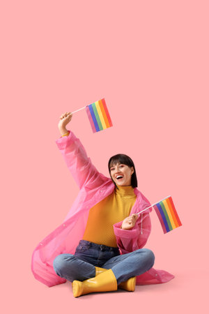 Beautiful young woman with LGBT flags sitting on pink backgroundの写真素材