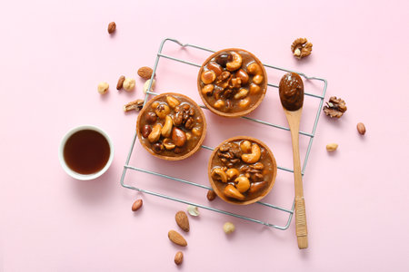 Tasty tarts with nuts and caramel sauce on stand against pink backgroundの写真素材