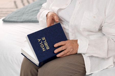 Senior woman with Bible sitting on bed at home, closeupの写真素材
