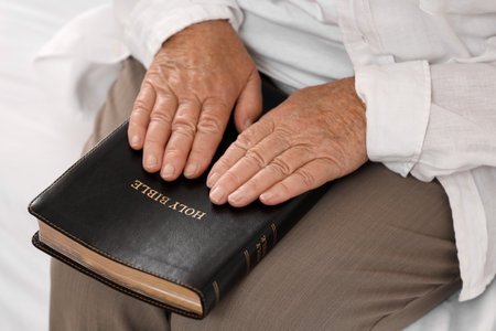 Senior woman with Bible sitting on bed at home, closeupの写真素材