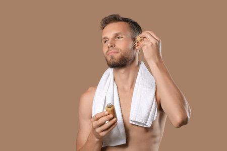 Handsome young man applying serum to his beard on brown backgroundの写真素材