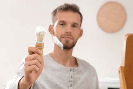 Bearded young man applying shaving foam with brush at homeの写真素材