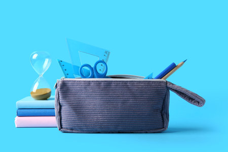 Gray pencil case with different stationery on blue background