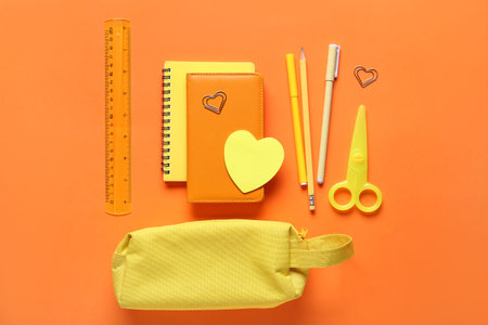 Yellow pencil case with different stationery on orange background. Top view