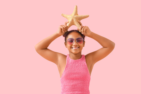 Happy African-American girl with starfish on pink backgroundの写真素材
