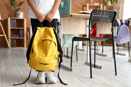 Little schoolboy with yellow backpack in classroomの写真素材