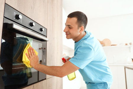 Young man cleaning oven in kitchenの写真素材