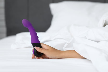 Female hand with vibrator on bed at home, closeupの写真素材