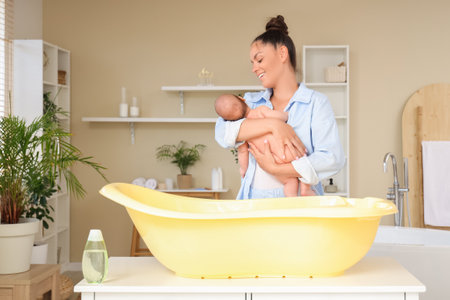 Beautiful young happy mother with cute little baby before bathing at homeの写真素材