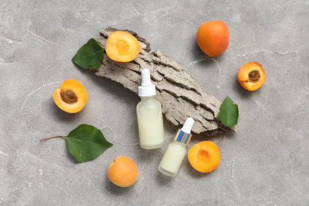 Bottles of cosmetic oil with fresh apricots and tree bark on gray backgroundの写真素材