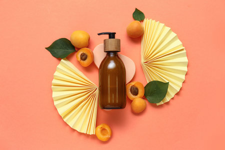 Decorative podium with bottle of cosmetic product and fresh apricots on orange backgroundの写真素材