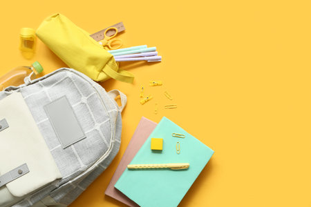 Modern school backpack with different stationery supplies and bottle of water on yellow backgroundの写真素材