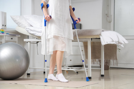 Female patient with crutches walking in hospital wardの写真素材