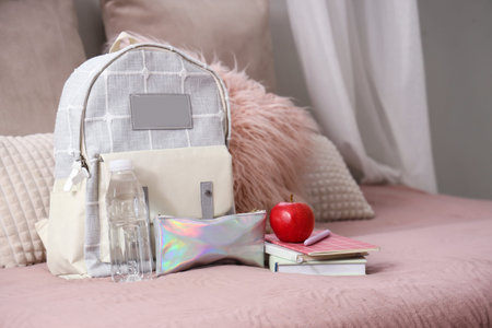 Backpack with apple, water bottle and books on bed in children's room