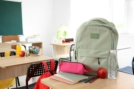 Backpack with apple, water bottle and pencil case on desk in classroomの写真素材