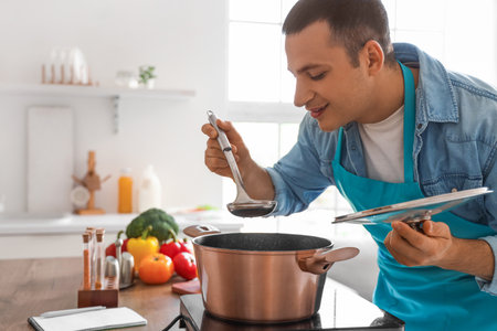 Young man tasting soup in kitchenの写真素材