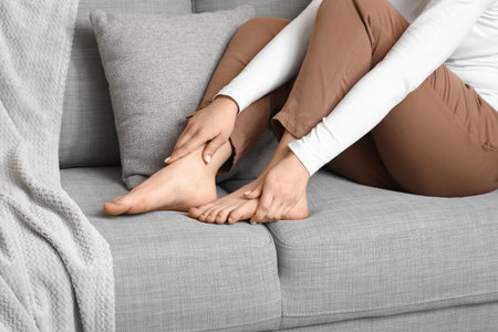 Young woman suffering from joint pain on sofa at homeの写真素材