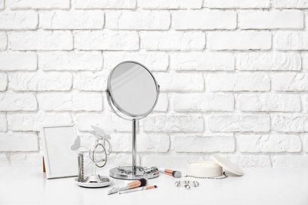 Stylish different jewelry with mirror and photo frame on table near white brick wallの写真素材