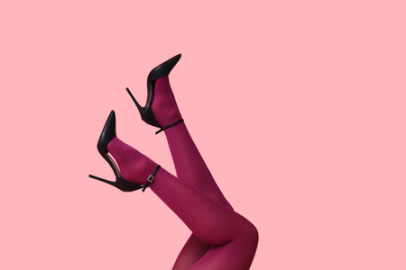 Legs of young woman in tights and high-heeled shoes on pink backgroundの写真素材