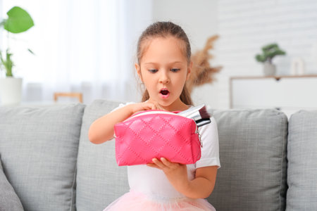 Cute little girl with cosmetic bag sitting on sofa in living roomの写真素材