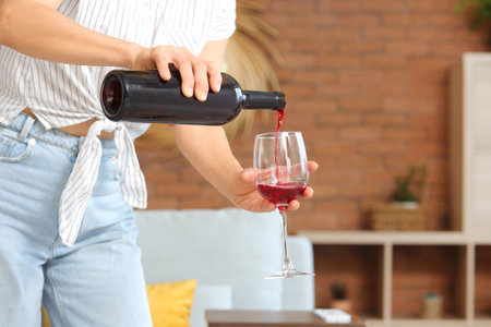 Woman pouring red wine from bottle into glass at home, closeupの写真素材