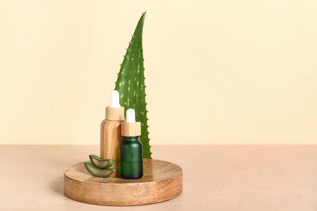 Fresh aloe leaf, wooden stand and bottles of essential oil on beige backgroundの写真素材