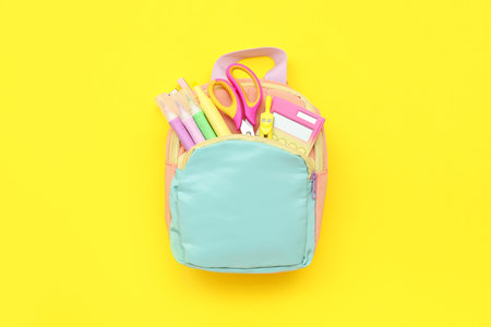 Blue school backpack with stationery on yellow backgroundの写真素材
