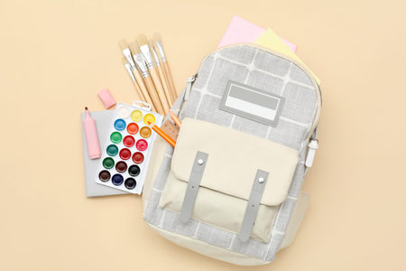 School backpack with paint brushes and palette on beige background
