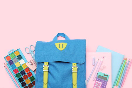 Blue school backpack with stationery, paint palette and books on pink backgroundの写真素材