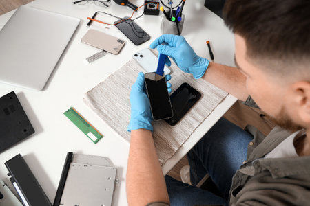 Male technician repairing mobile phone at table in service center, closeupの写真素材