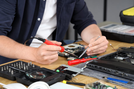 Male technician with soldered iron repairing laptop in service center, closeup