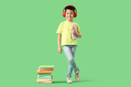 Cute little Asian boy in headphones listening to audiobook with books on green backgroundの写真素材