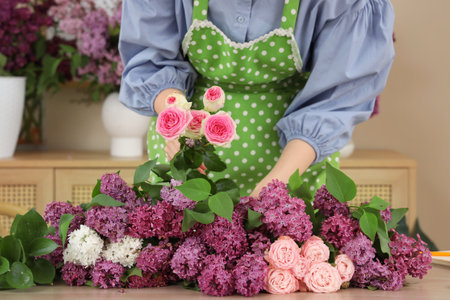 Female florist making beautiful bouquet with lilacs and roses in flower shopの写真素材