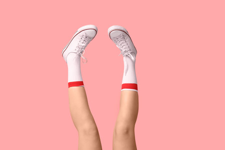 Legs of young woman in socks and white sneakers on pink backgroundの写真素材