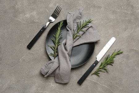 Modern table setting with napkin, cutlery and rosemary on gray grunge backgroundの写真素材