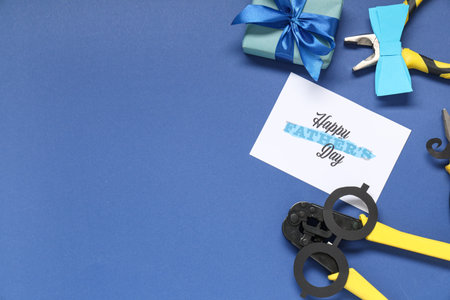 Pliers, gift box and paper with text HAPPY FATHER'S DAY on blue background. Top view