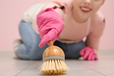 Young woman cleaning floor with brush on pink background, closeupの写真素材
