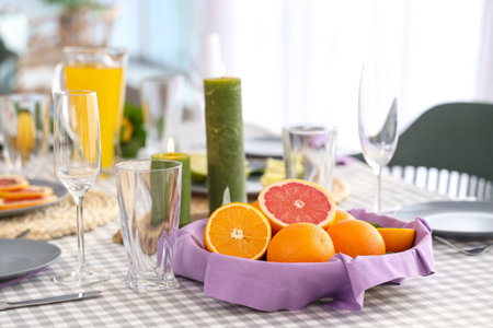 Beautiful table setting with citrus fruits and candles on checkered tablecloth in living room