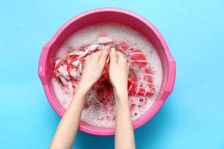 Woman washing clothes in plastic basin on blue backgroundの写真素材