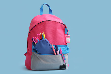 Pink school backpack with stationery on blue background