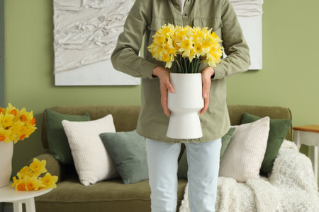 Woman holding vase with daffodils at homeの写真素材
