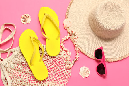 Flip flops with string bag, straw hat, sunglasses and seashells on pink backgroundの写真素材