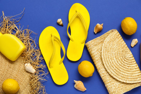 Flip flops with lemons, bottle of sunscreen and straw bag on blue background