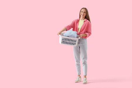 Young woman holding basket with clothes on pink backgroundの写真素材