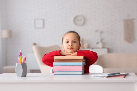 Cute little girl with books sitting by table and studying at homeの写真素材